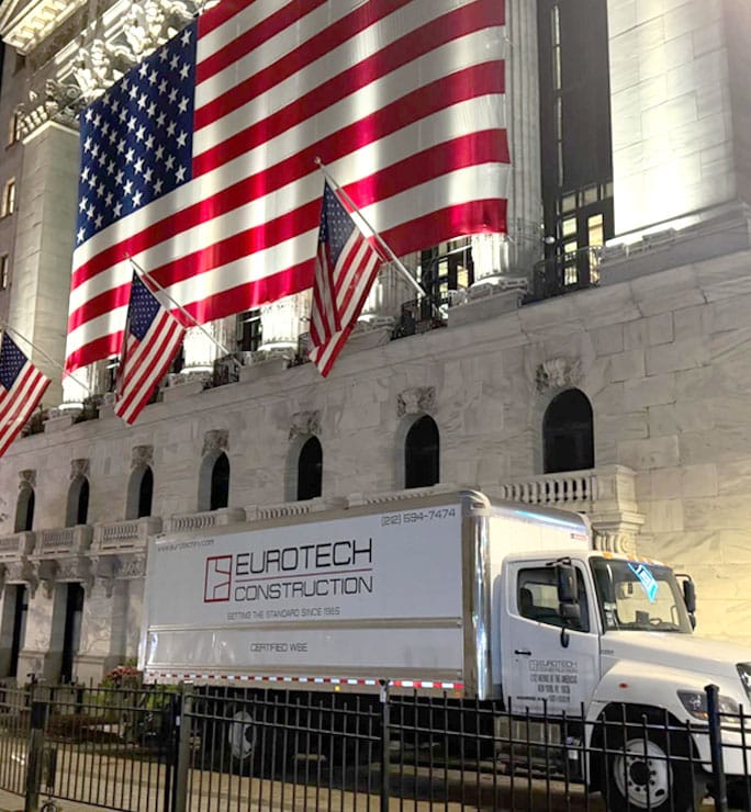 Eurotech Construction truck parked outside a large building with multiple American flags.