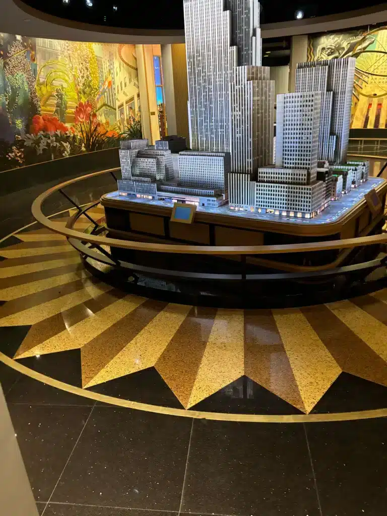 A detailed scale model of the Empire State Building is displayed in a museum, surrounded by a golden star-patterned floor and colorful mural walls.