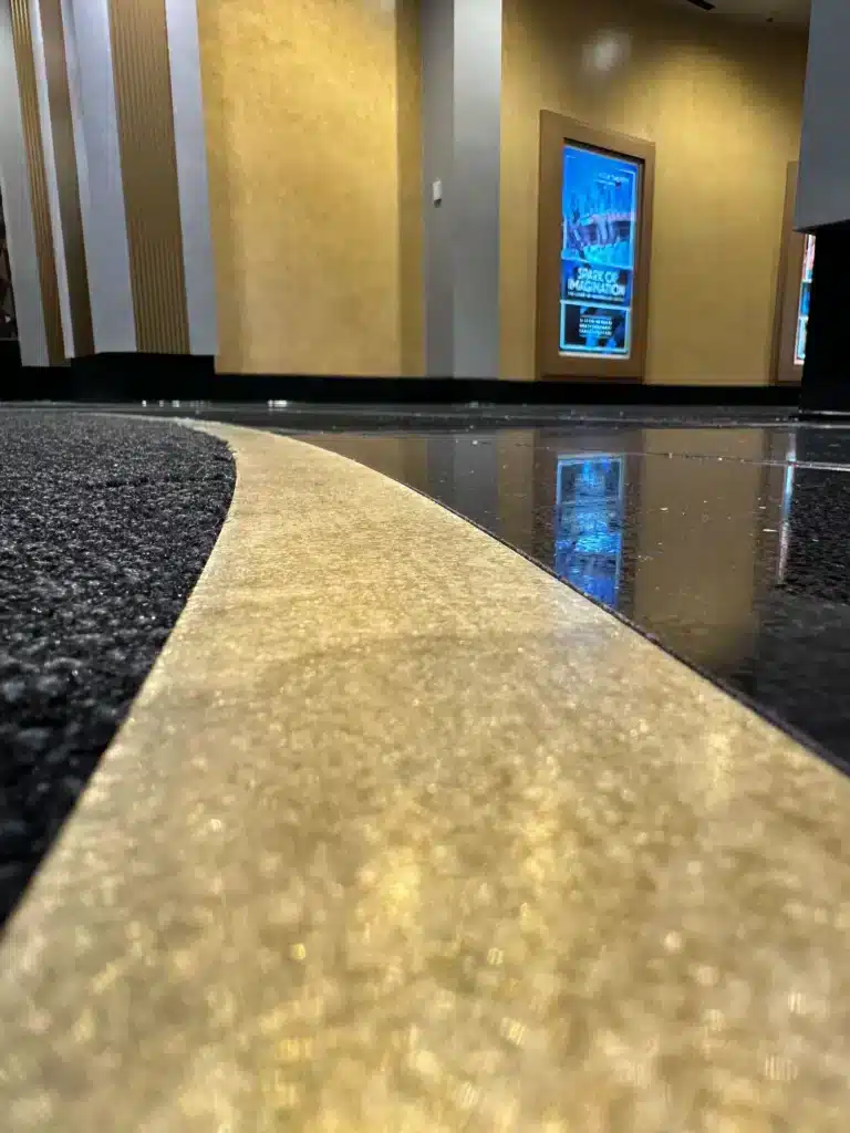 A low-angle view of a shiny black and gold floor inside a building, with gold walls, a movie poster on the wall, and modern architectural details in the background.