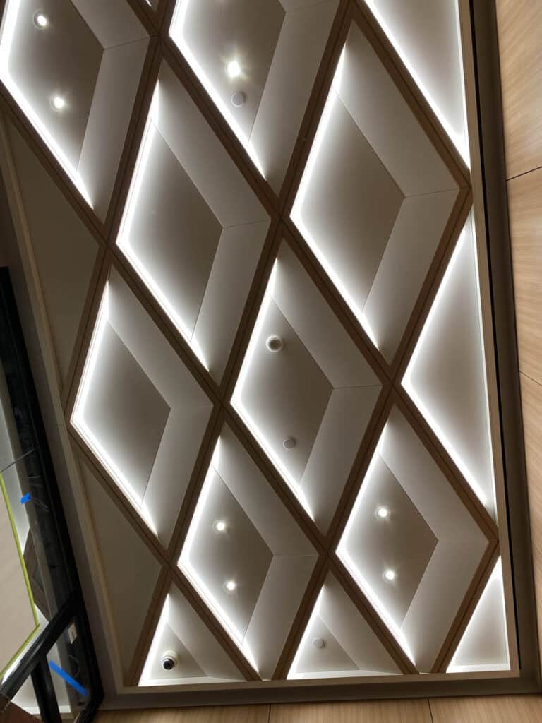 Ceiling with a grid of diamond-shaped panels, each outlined by bright, recessed lighting and containing a central light fixture, giving a geometric, modern look.
