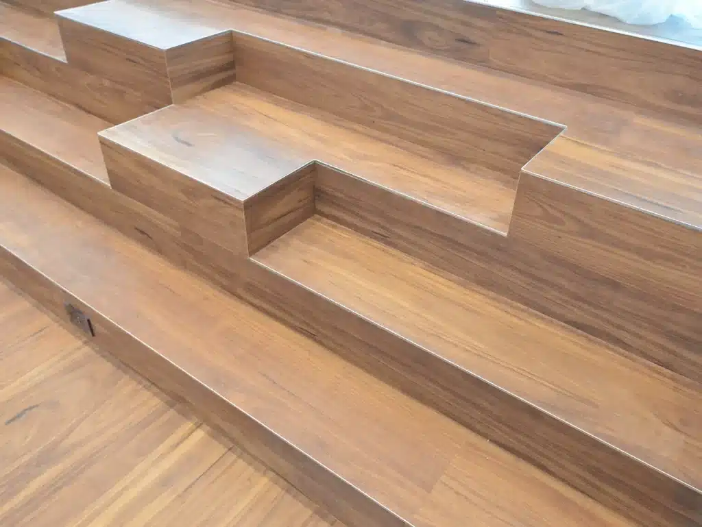 Wide wooden stairs featuring alternating step heights and depths, creating an unusual, staggered pattern. The steps appear to be made from polished wood with visible grain patterns.