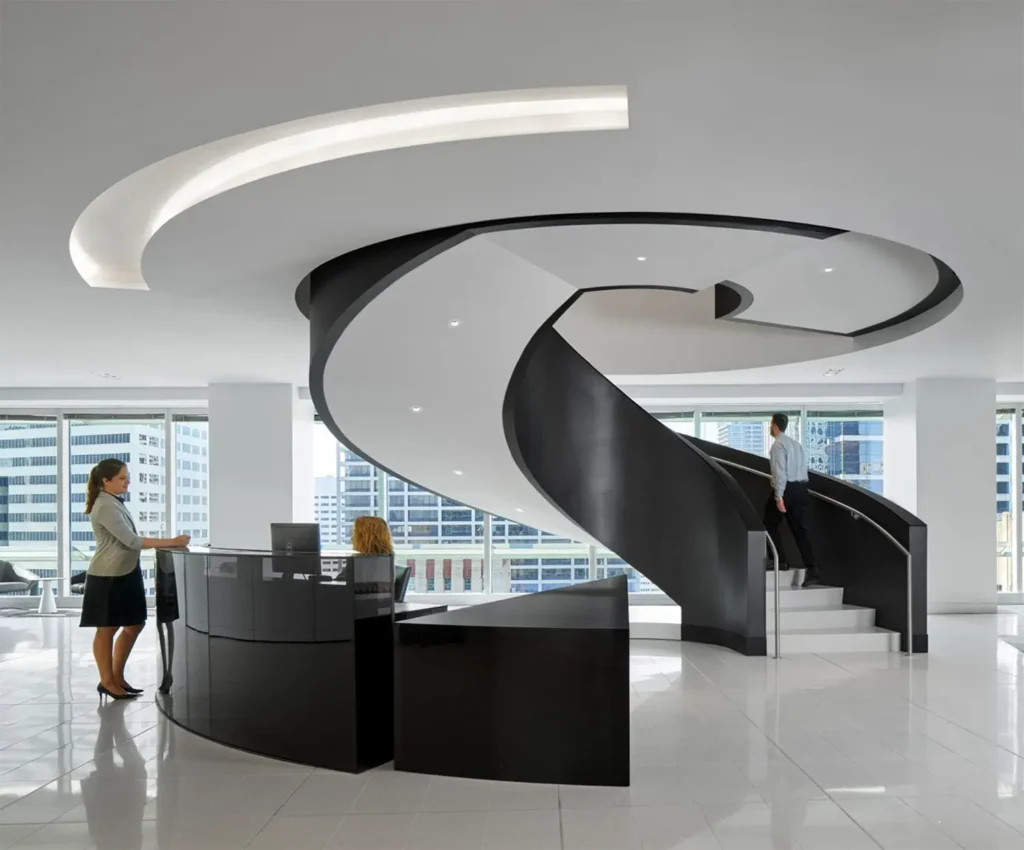 Modern office lobby with a black spiral staircase, a curved reception desk with a seated receptionist, large windows showing city buildings, and two people interacting in the bright, open space.
