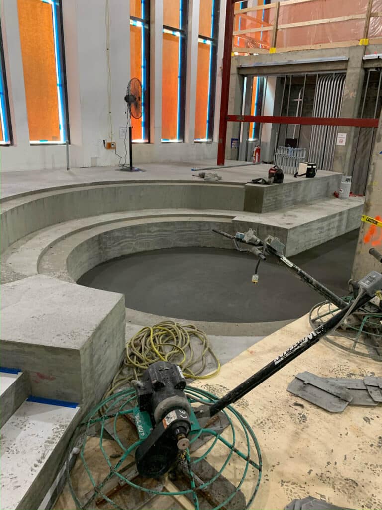 A circular concrete structure under construction, possibly a pool or fountain, with power tools, extension cords, and construction materials scattered around the unfinished area.